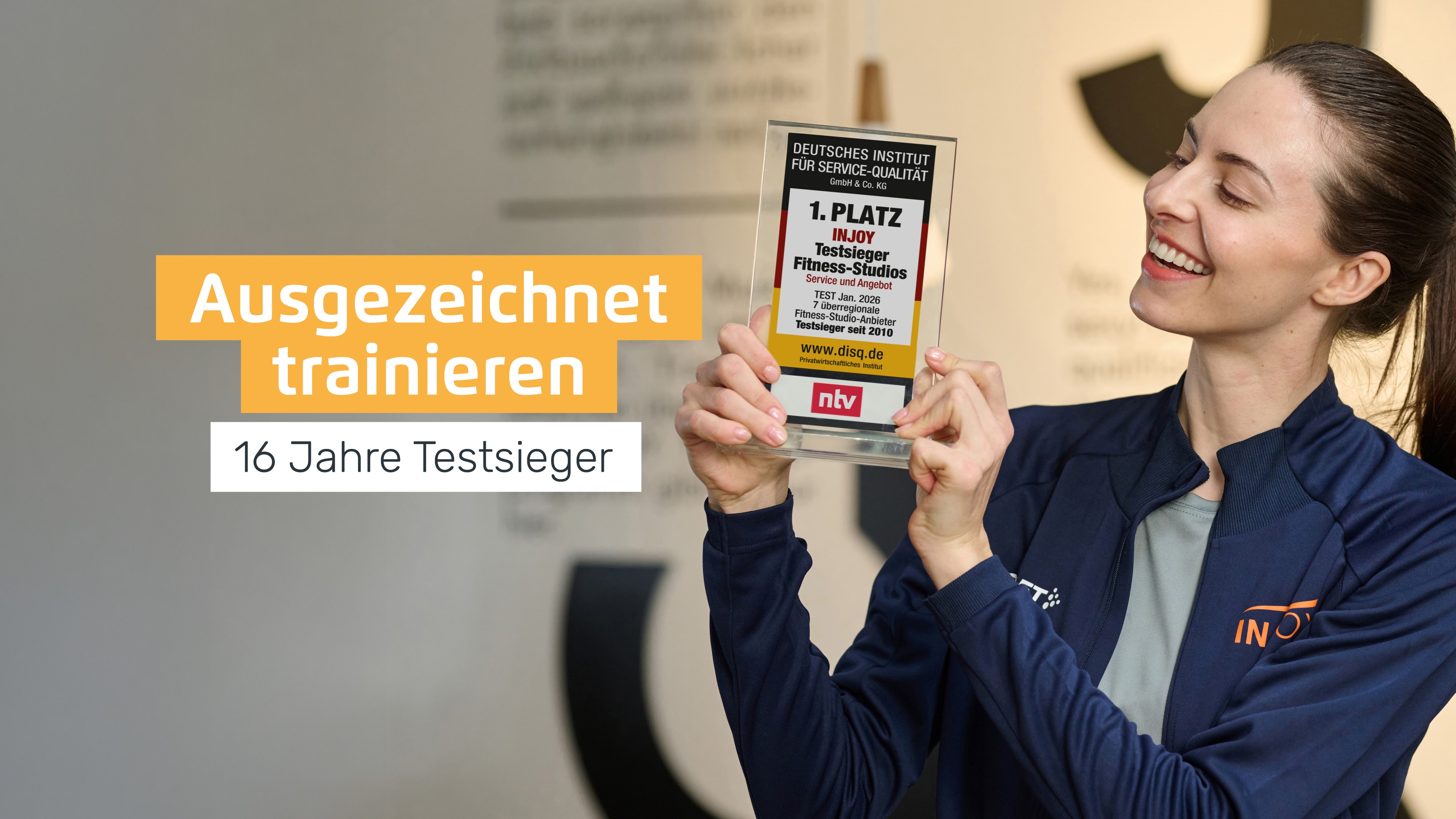 Eine gut gelaunte INJOY Trainerin präsentiert den aktuellen INJOY Testsieger Award "Fitnessstudio 2026".