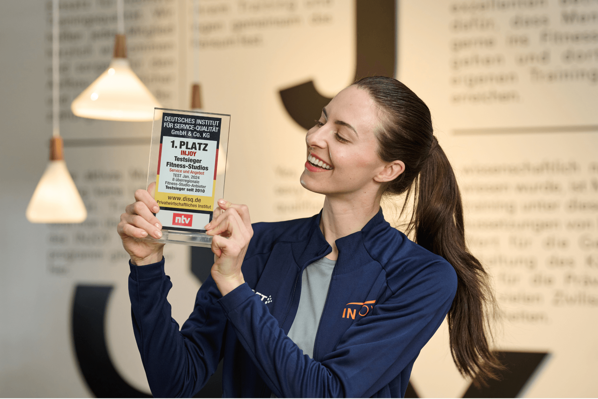Eine fröhliche INJOY Trainerin hält stolz den Testsieger-Award in Händen.
