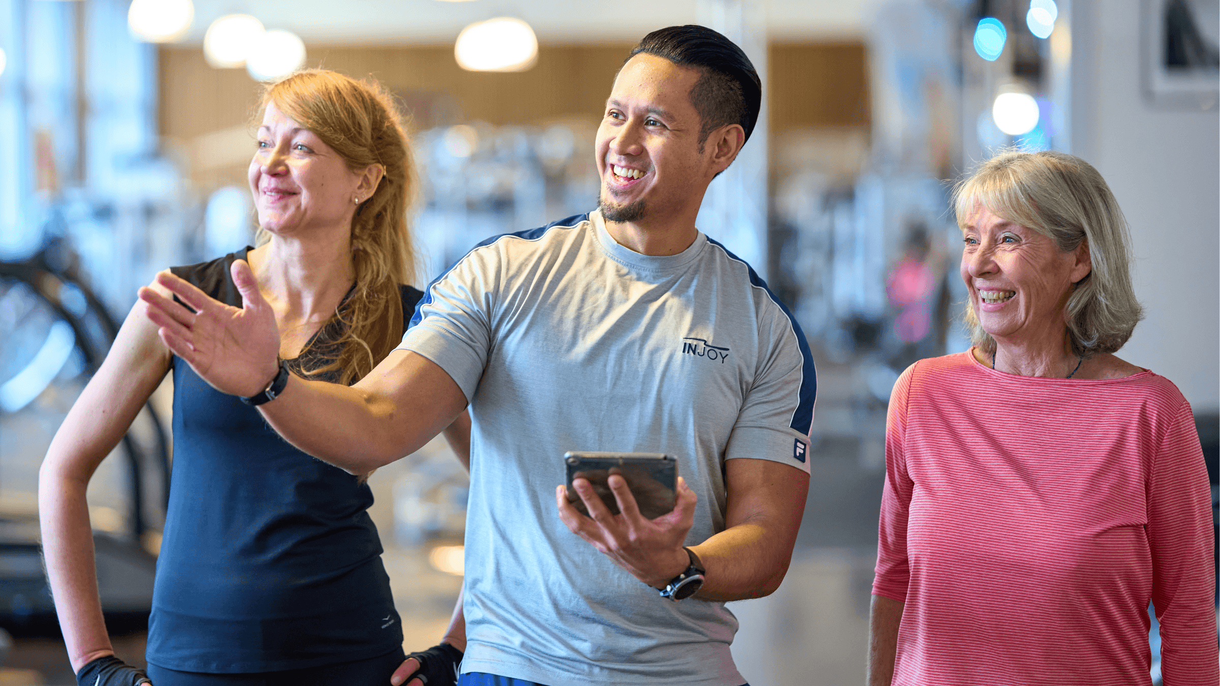 Eine motivierter Trainer des INJOY Fitnessstudios Hagen zeigt zwei Mitgliedern den Cardiobereich des Studios.