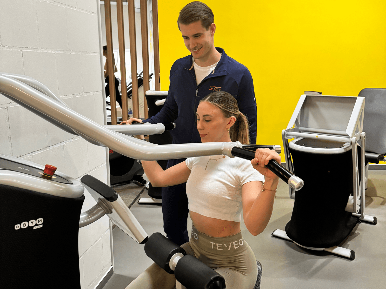 Eine Frau sitzt an einem eGym-Gerät im INJOY Fitnessstudio Rudolstadt und führt mit Trainer das Testprogramm durch.