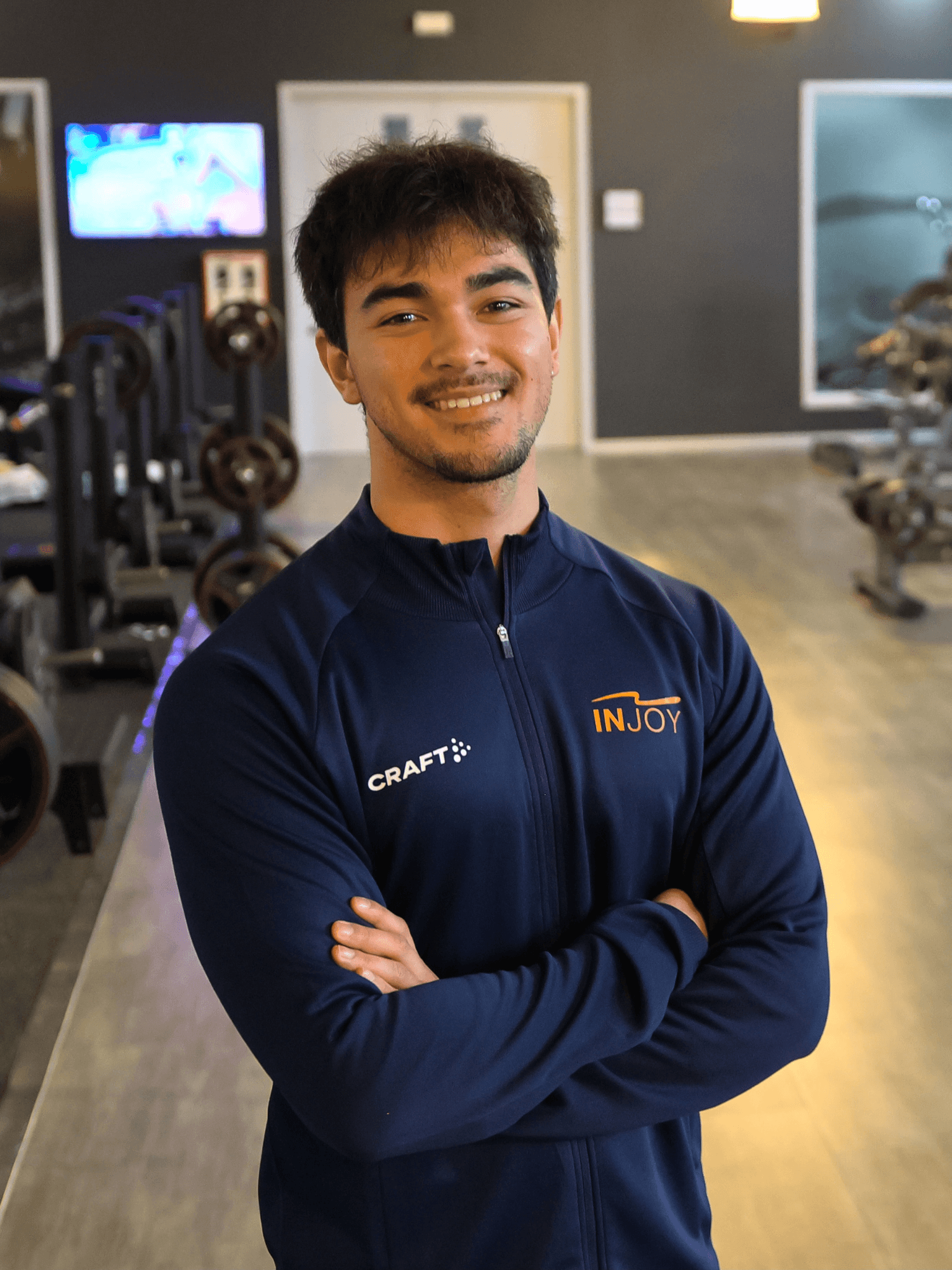 Ein Trainer des INJOY Fitnessstudios in Hagen lächelt stolz und mit verschränkten Armen in die Kamera.