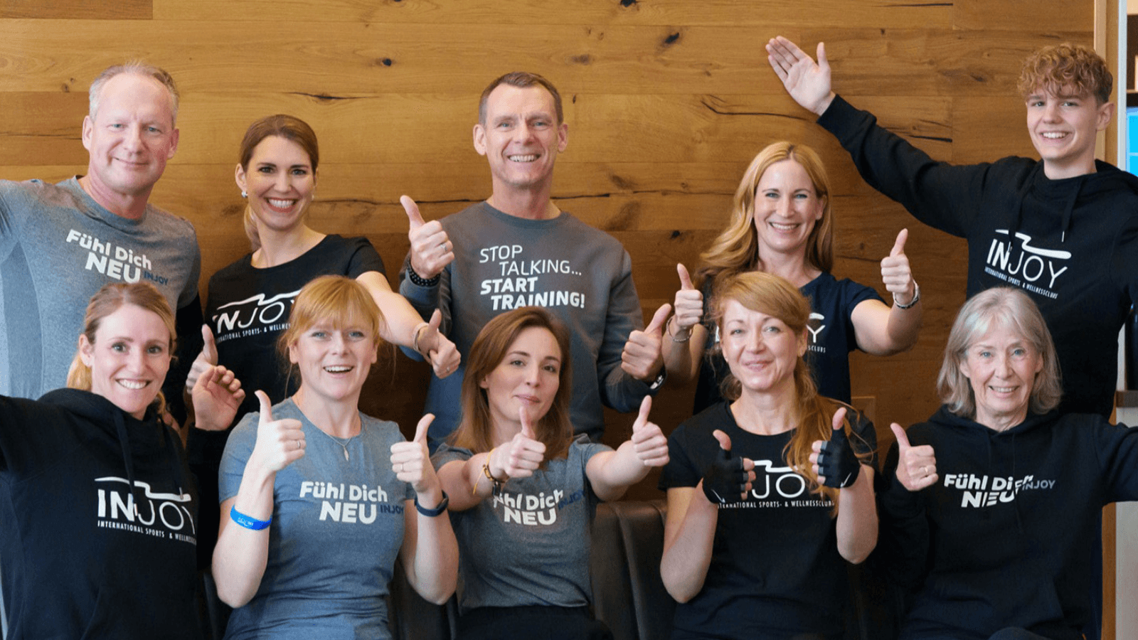 Das Team des INJOY Fitnessstudios Hagen-Hohenlimburg posiert für ein Gruppenfoto. Alle Mitglieder zeigen einen Daumen nach oben und lachen in die Kamera