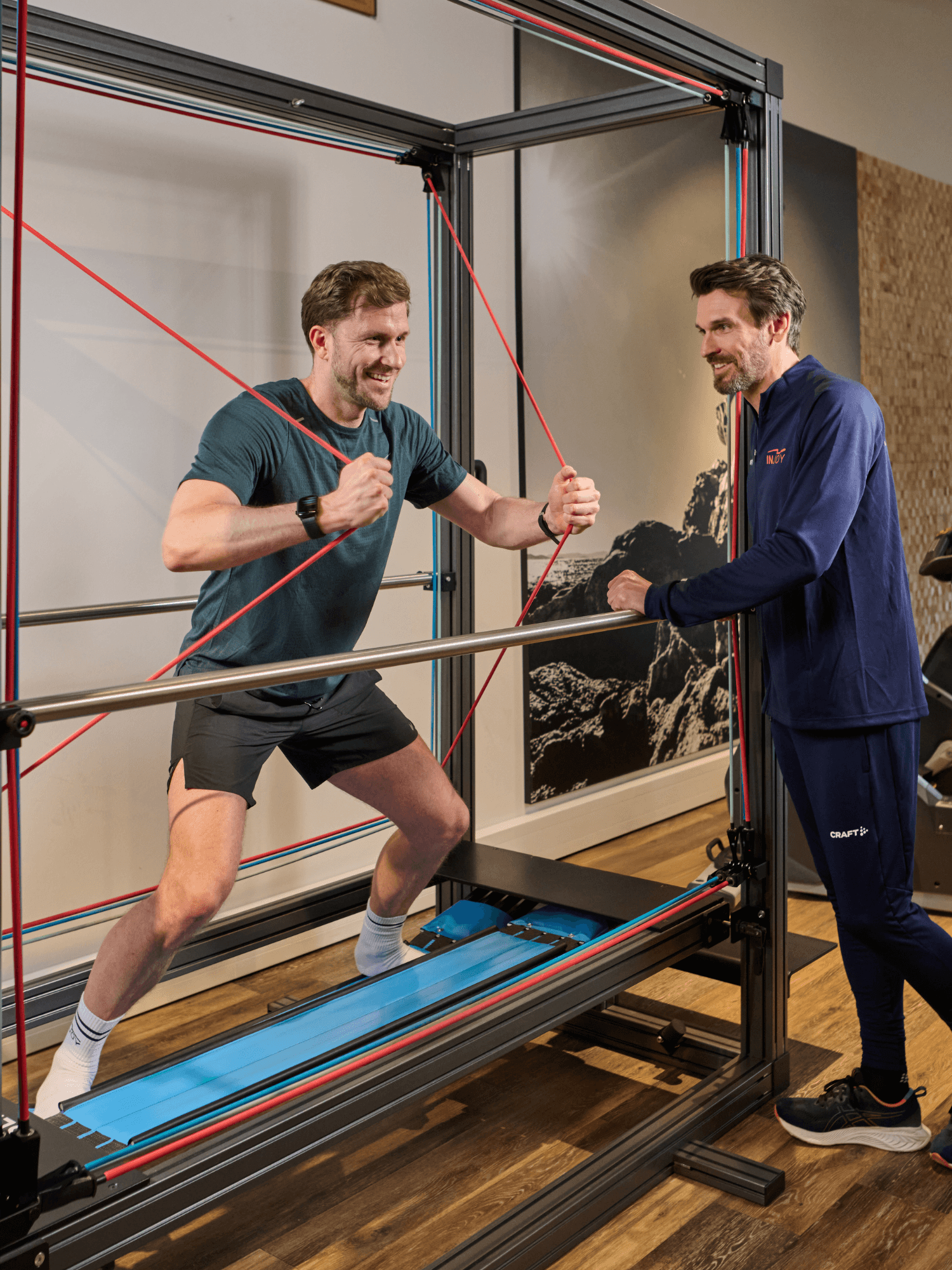Ein männliches INJOY Mitglied trainiert am Sensopro und erhält dabei hilfreiche Tipps von einem INJOY Trainer.