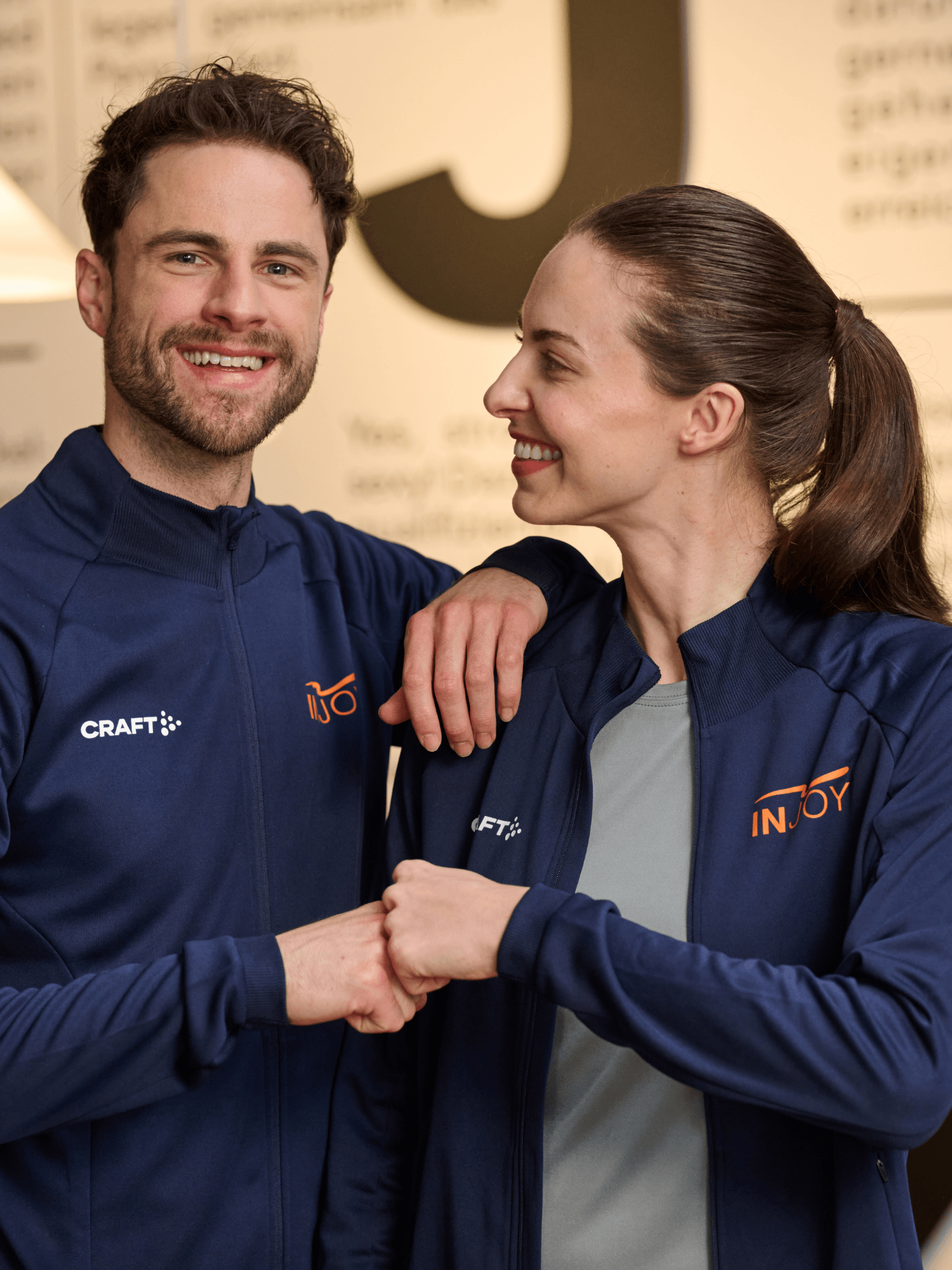 Ein INJOY Mitarbeiter und eine INJOY Mitarbeiterin geben sich einen fist bump und der männliche Mitarbeiter lacht dabei in die Kamera.