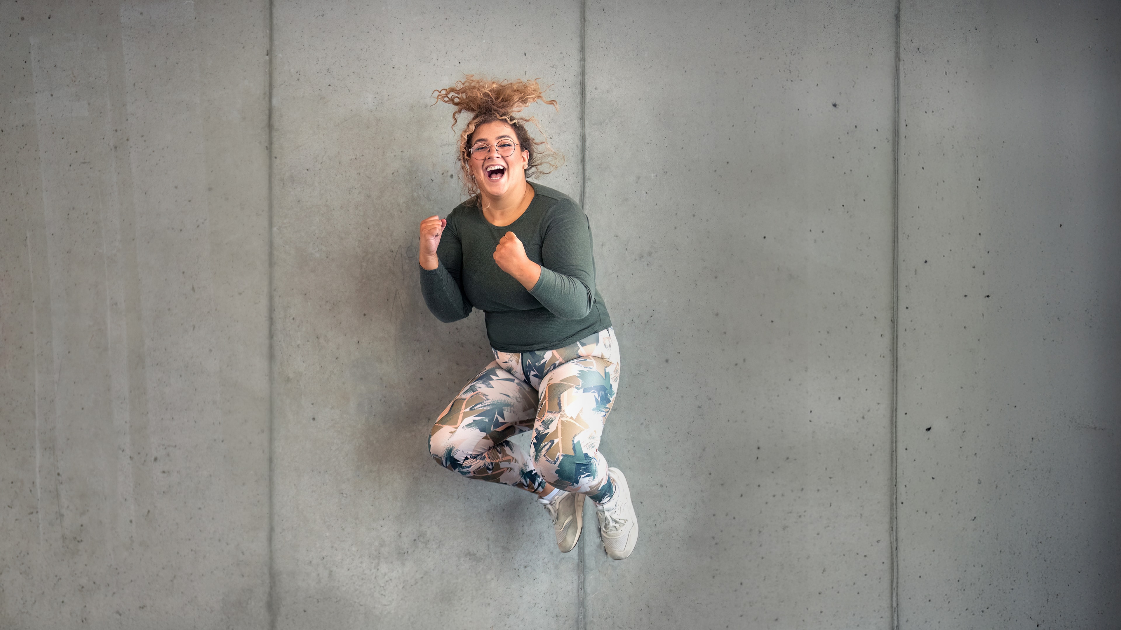 Ein INJOY Fitnessstudio Mitglied springt vor Glück in die Luft und lacht dabei in die Kamera.