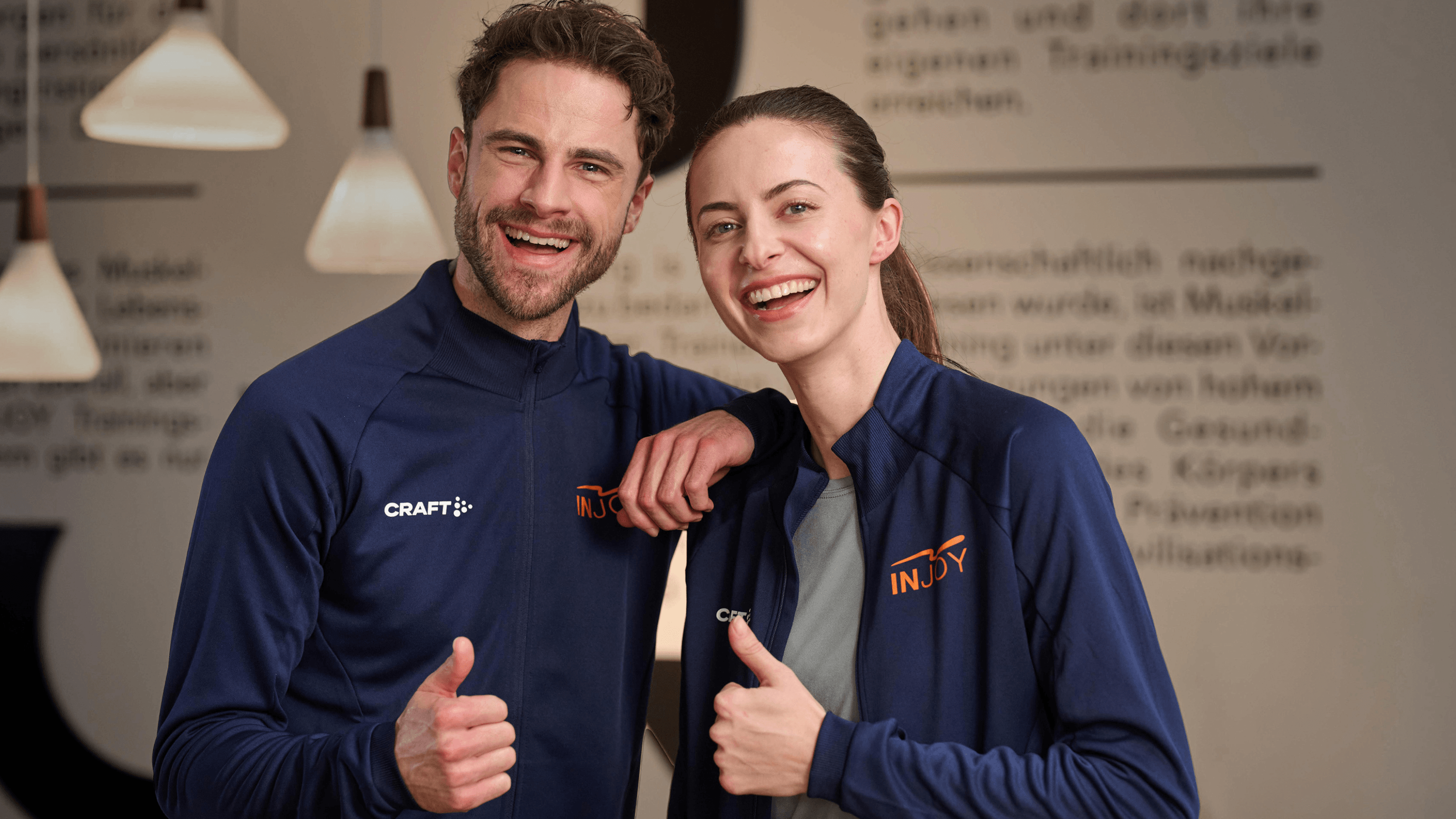 Zwei INJOY Trainer lächeln in die Kamera und zeigen einen Daumen nach oben.