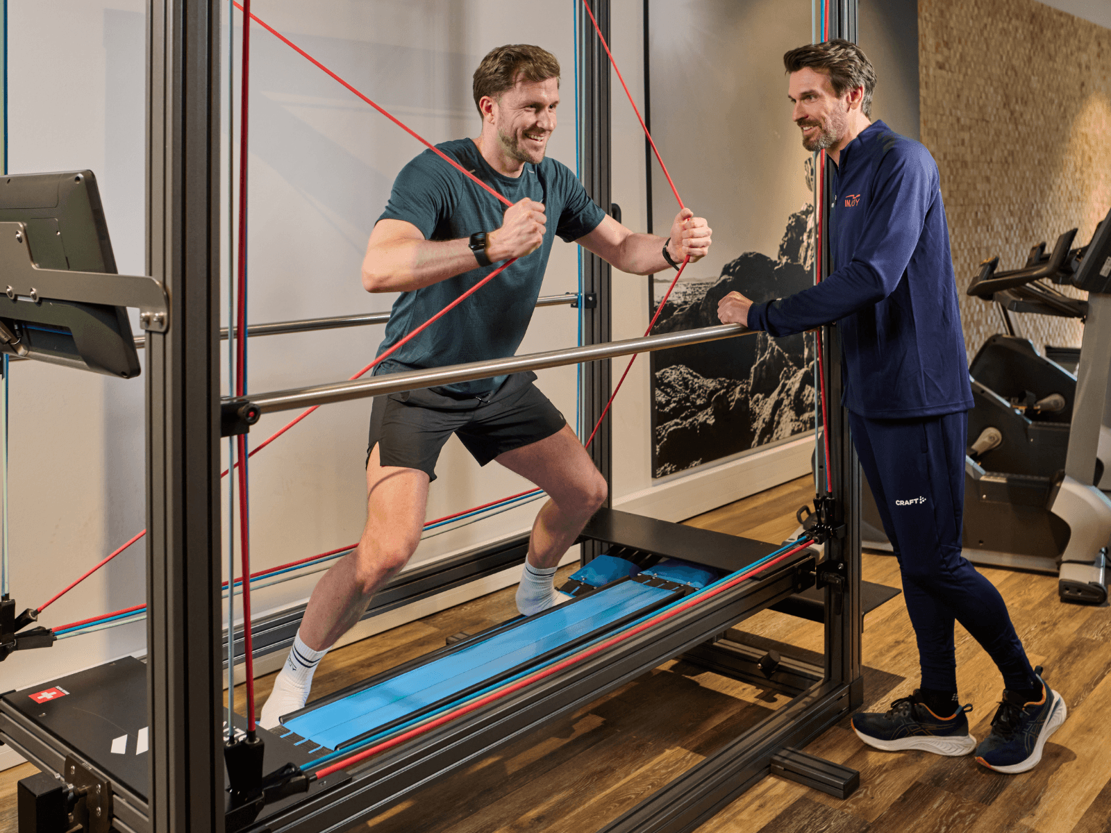 Ein junges INJOY Mitglied steht auf einem Sensopro im Fitnessstudio und wird dabei von einem erfahrenen Trainer betreut.