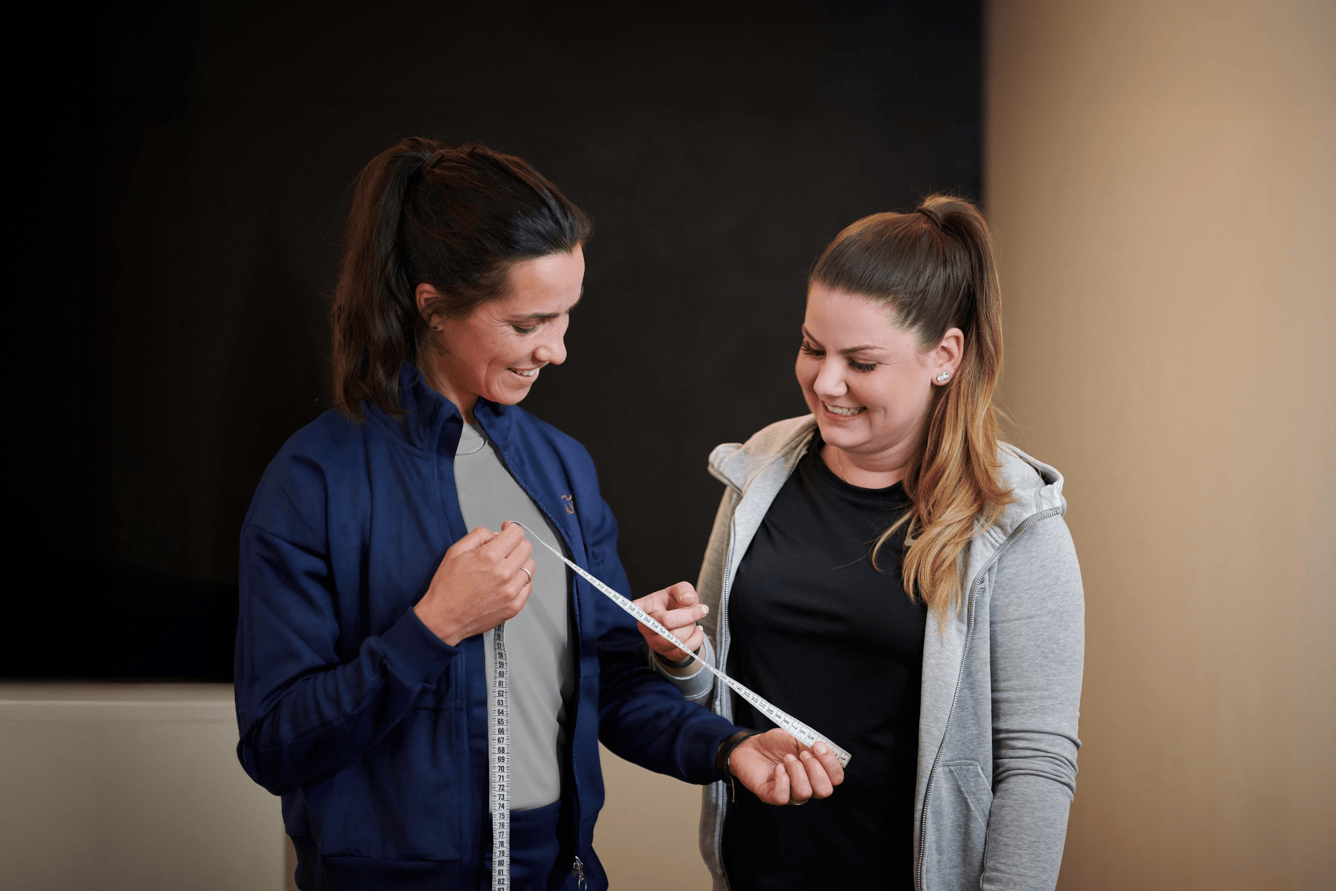 Eine INJOY Trainerin und ein weibliches INJOY Mitglied stehen nebeneinander und bestaunen stolz das erreichte Abnehmziel des Mitglieds.