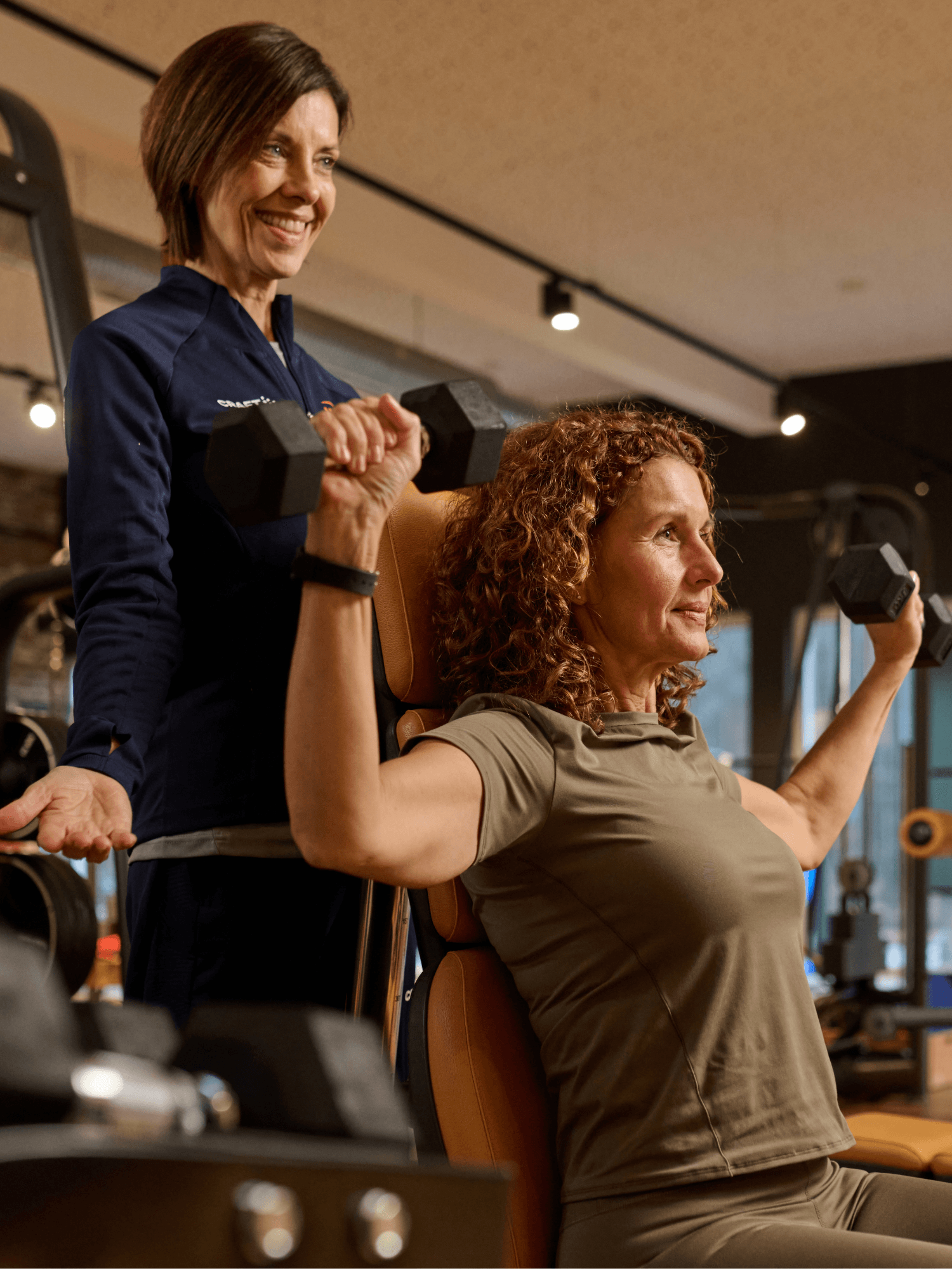 Eine weibliche INJOY Trainerin unterstützt ein INJOY Mitglied bei der Ausführung einer Schulterübung.