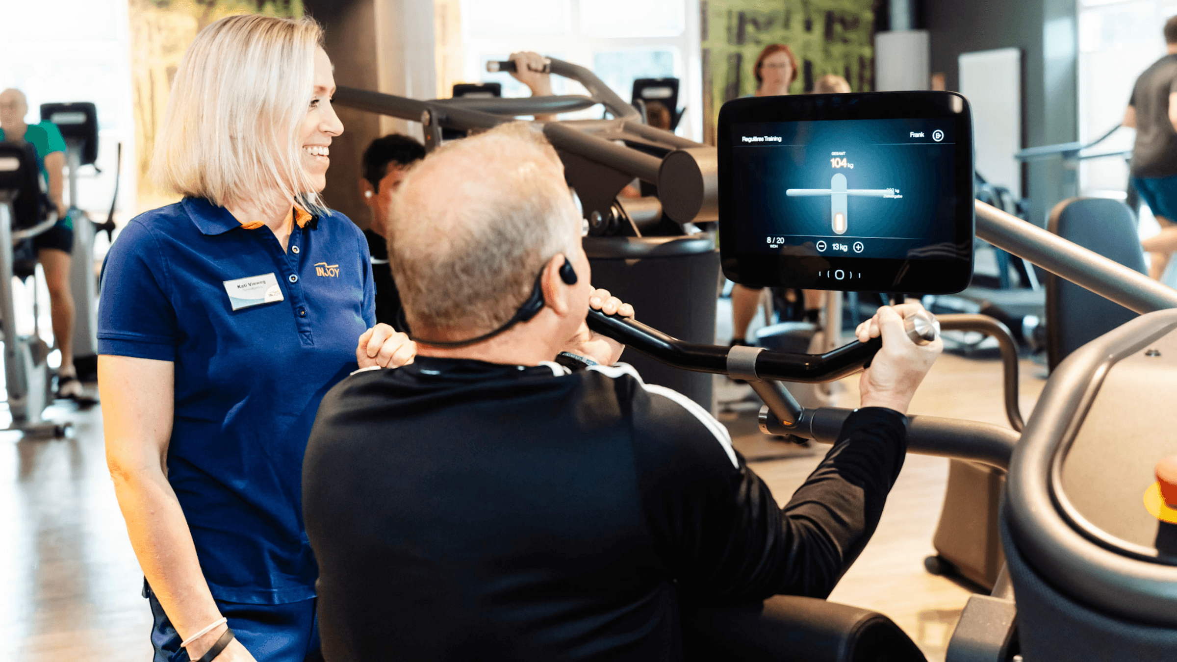 Eine INJOY Trainerin betreut ein Mitglied an einem EGYM Gerät im Fitnessstudio.