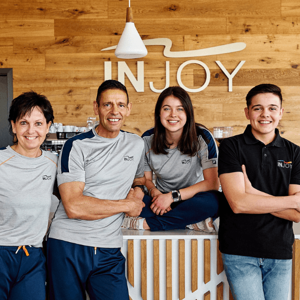 Das vierköpfige Team vom INJOY Balingen steht selbstbewusst vor dem INJOY Logo und lächelt in die Kamera.