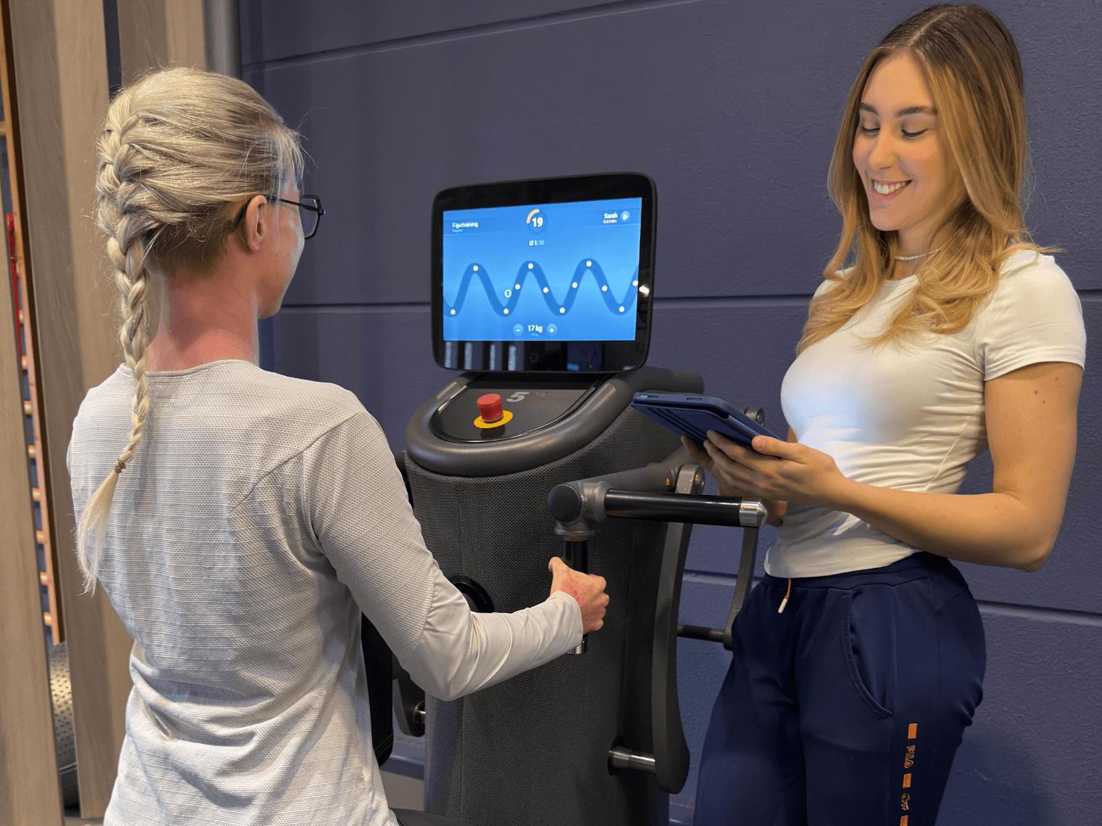 Eine Frau an einem eGym Zirkel-Trainingsgerät im INJOY Fitnessstudio Rudolstadt und lässt sich von einer Trainerin mit Tablet in der Hand beraten.