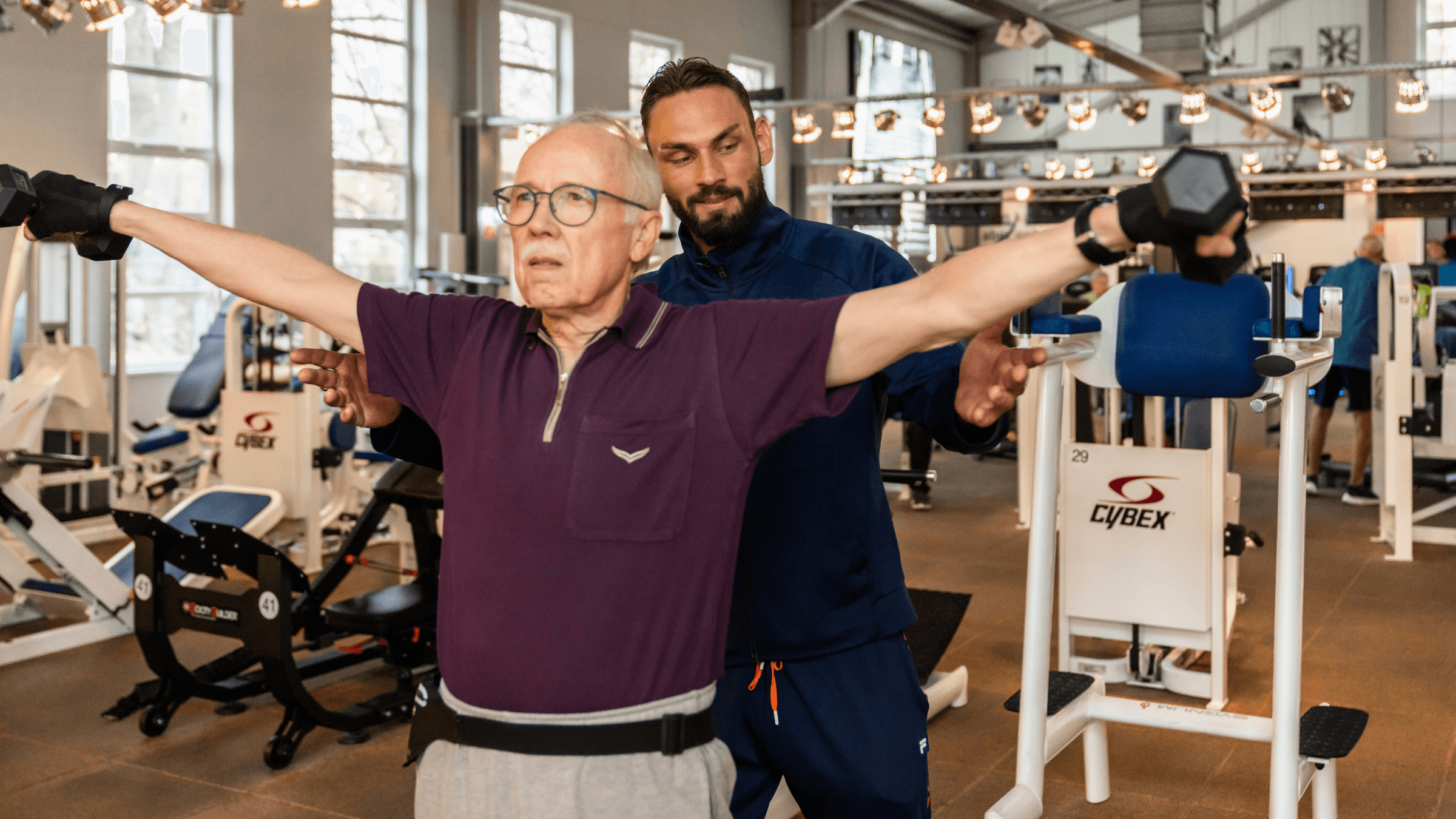 Ein INJOY Mitglied wird im Fitnessstudio INJOY Berlin-Steglitz von einem Trainer bei einer Schulterübung unterstützt.