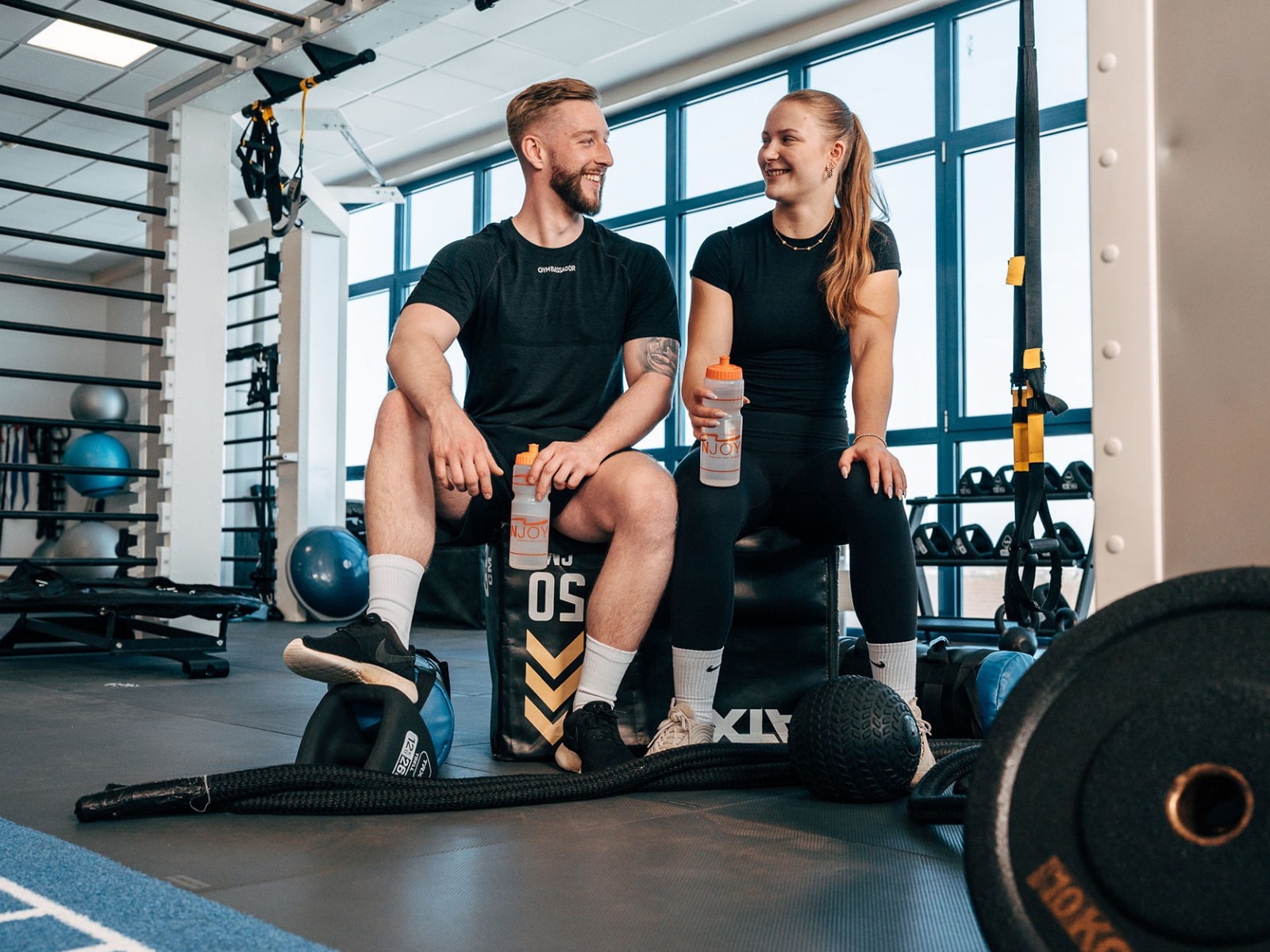 Ein Mann und eine Frau sitzen auf einem Cube innerhalb eines Functional Bereichs im Fitnessstudio INJOY Wolfsburg und schauen sich lächelnd an