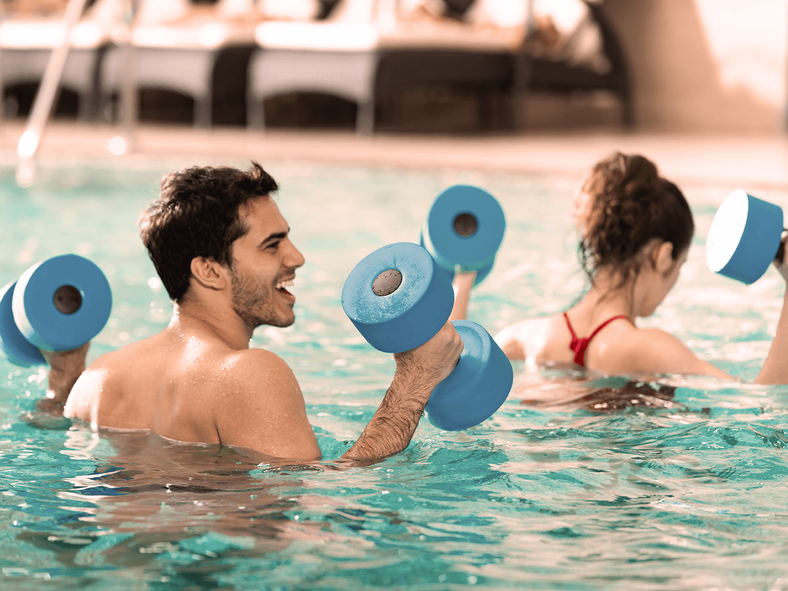 Zwei INJOY Mitglieder nehmen an einem Aqua-Kurs teil und heben spezielle Hanteln aus dem Wasser.