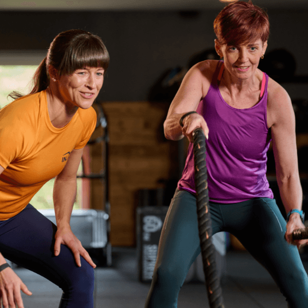 Ein INJOY Mitglied trainiert an den Battle-Ropes und wird dabei von einer INJOY Trainerin angefeuert.