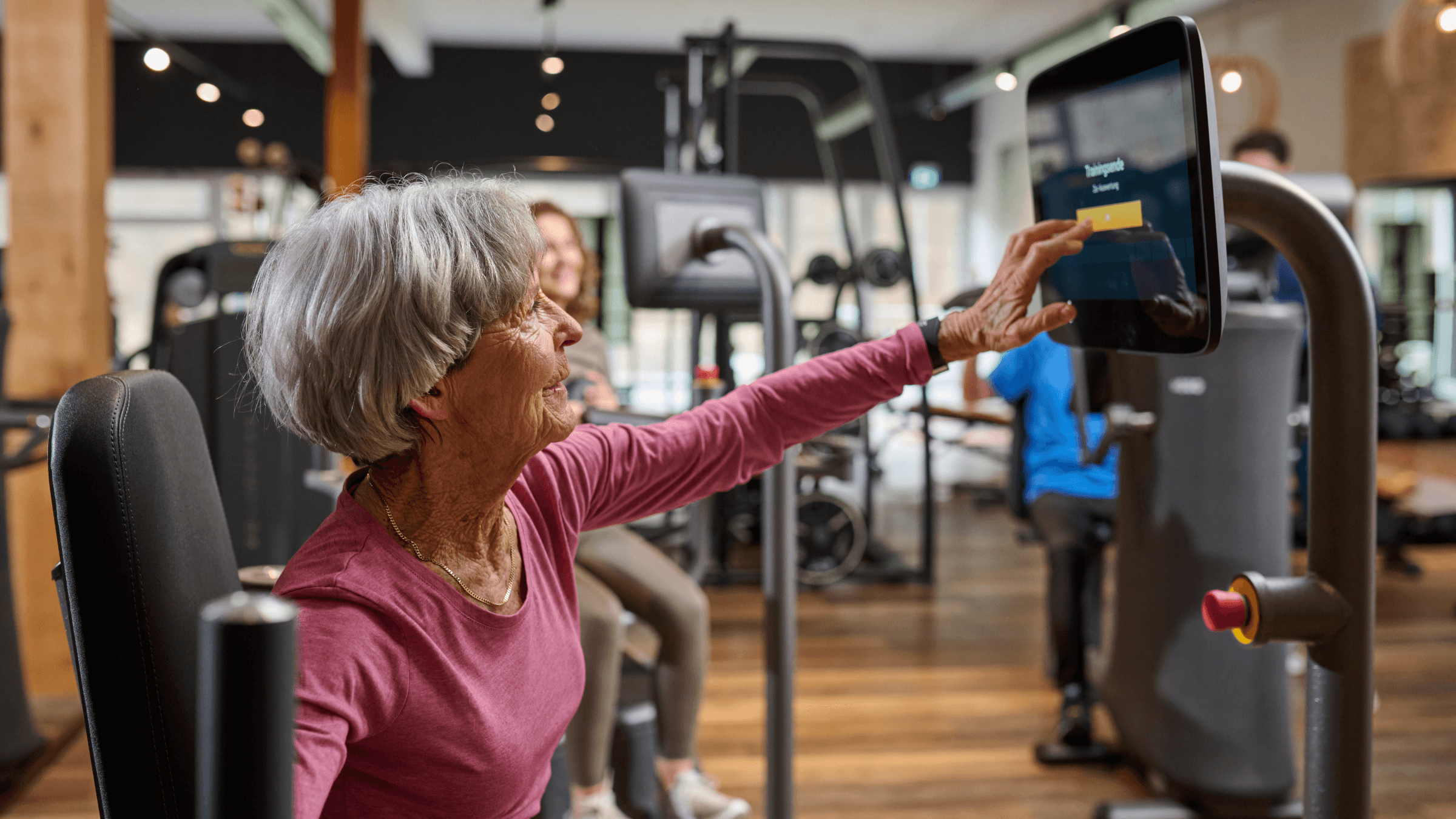 Ein älteres Mitglied sitzt im Fitnessstudio an einem EGYM Gerät und beginnt ihr Training.