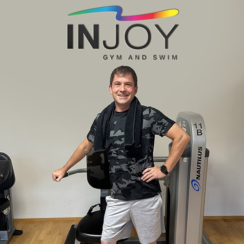 Ein männliches INJOY Gym and Swim Mitglied steht selbstbewusst vor einem Fitnessgerät und lächelt in die Kamera.