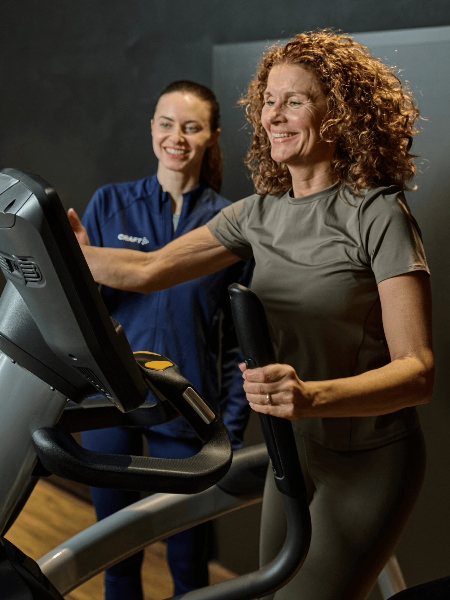 Eine INJOY Trainerin gibt einem weiblichen Mitglied eine Einweisung auf dem Crosstrainer im Fitnessstudio.