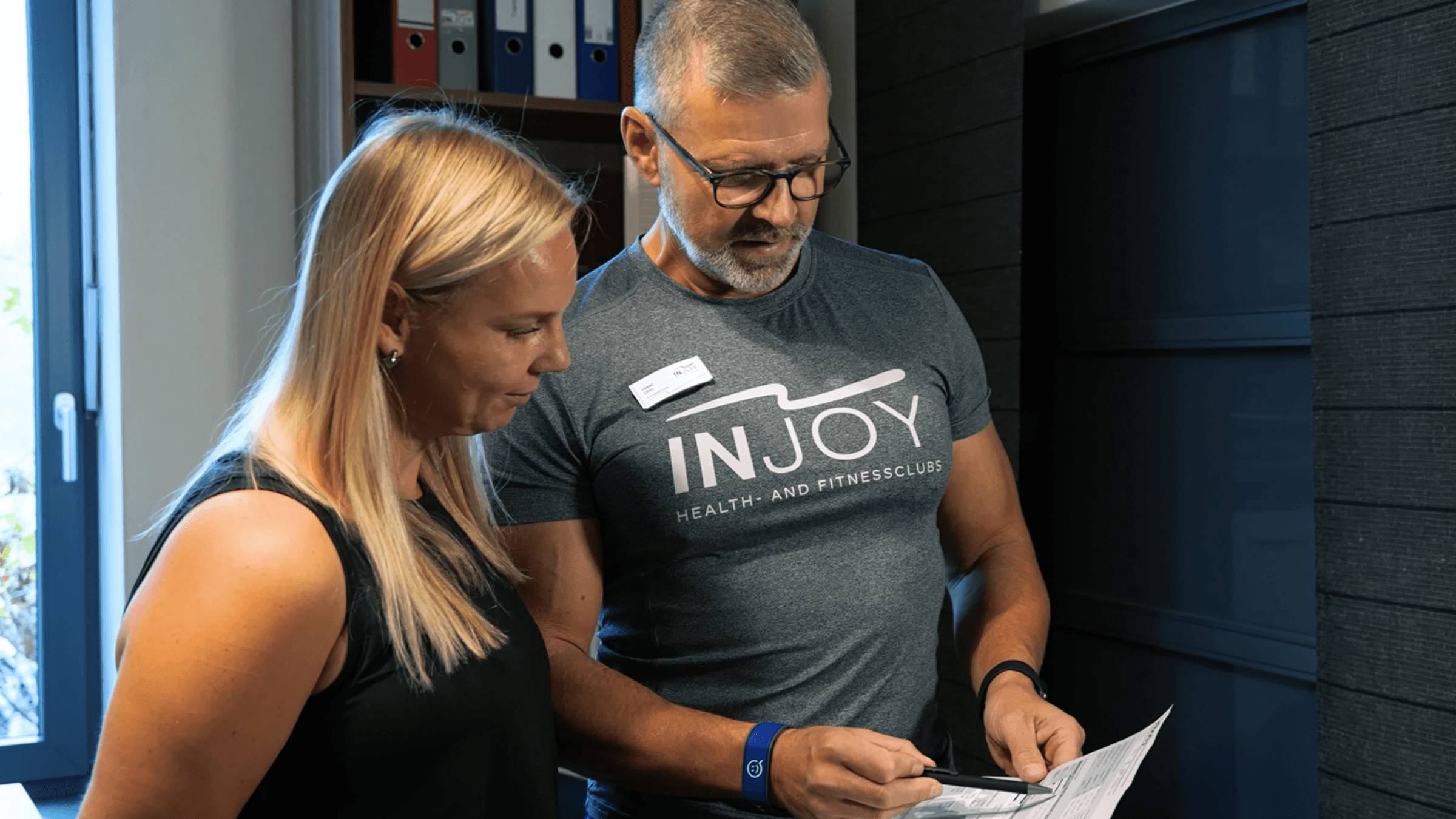 Trainer mit einem Informationsblatt berät eine Frau im INJOY Fitnessstudio Schwandorf.
