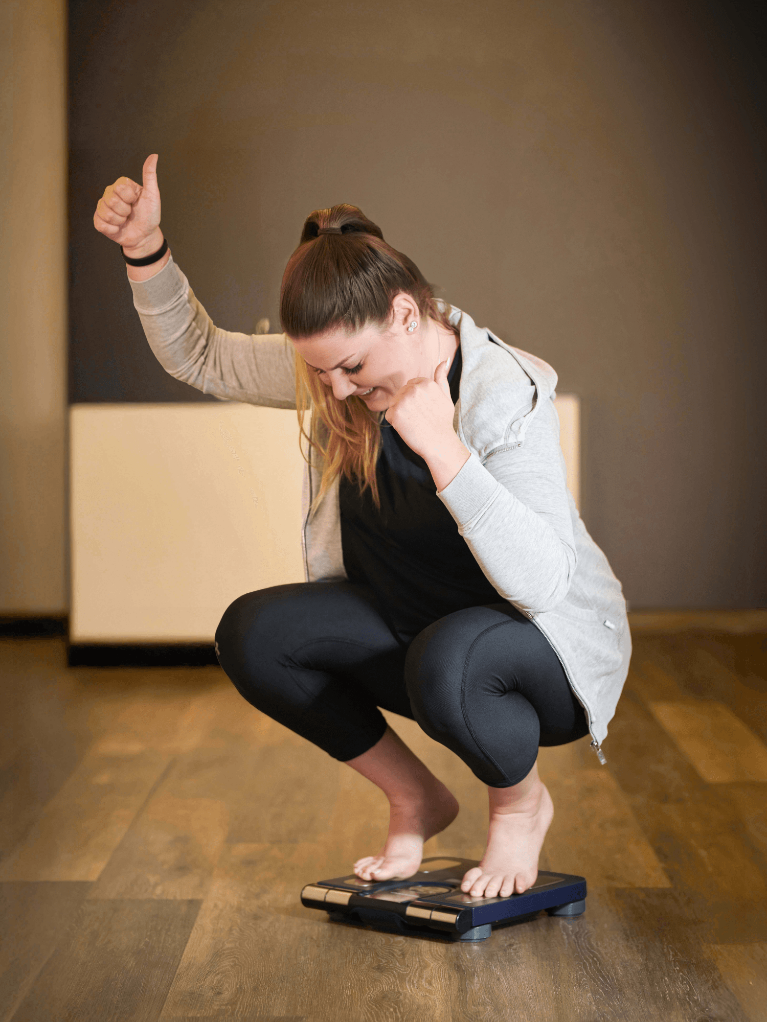 Ein glückliches INJOY Mitglied hebt einen Daumen nach oben, als sie ihr Ergebnis auf der Waage sieht.