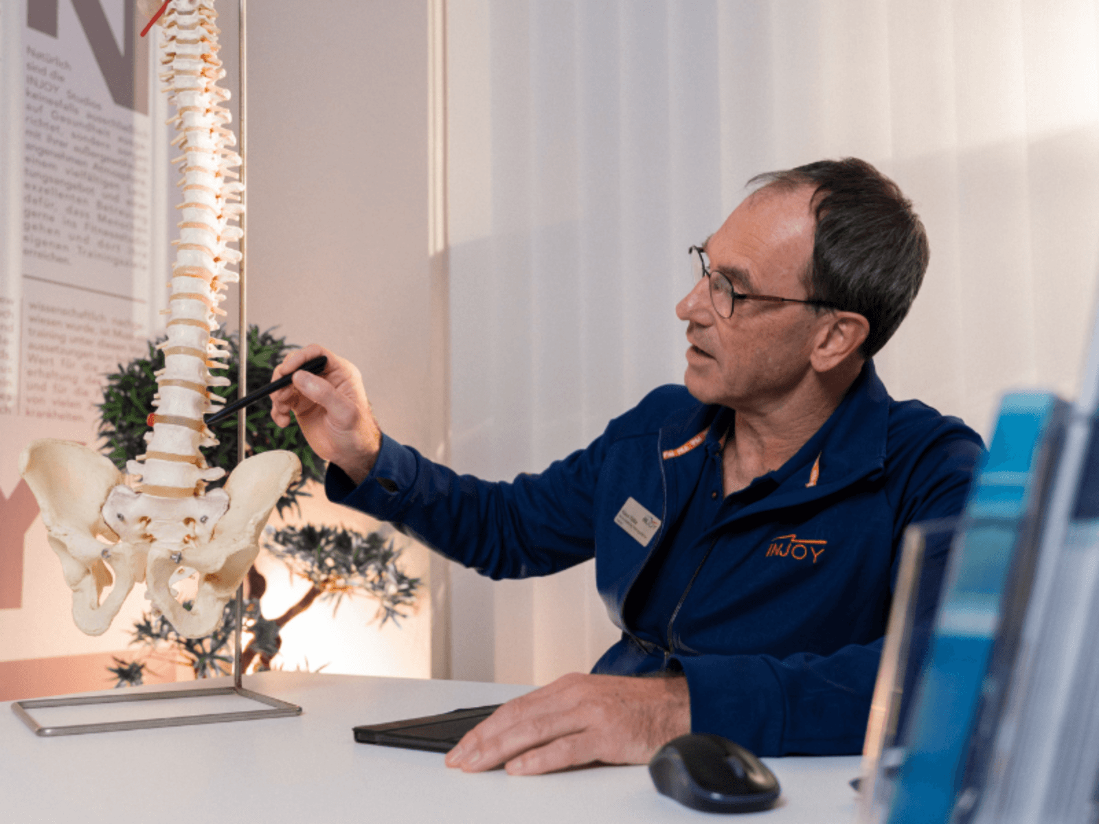 Ein INJOY Fitnessstudio Lohne Trainer vor einem Wirbelsäulen-Modell.