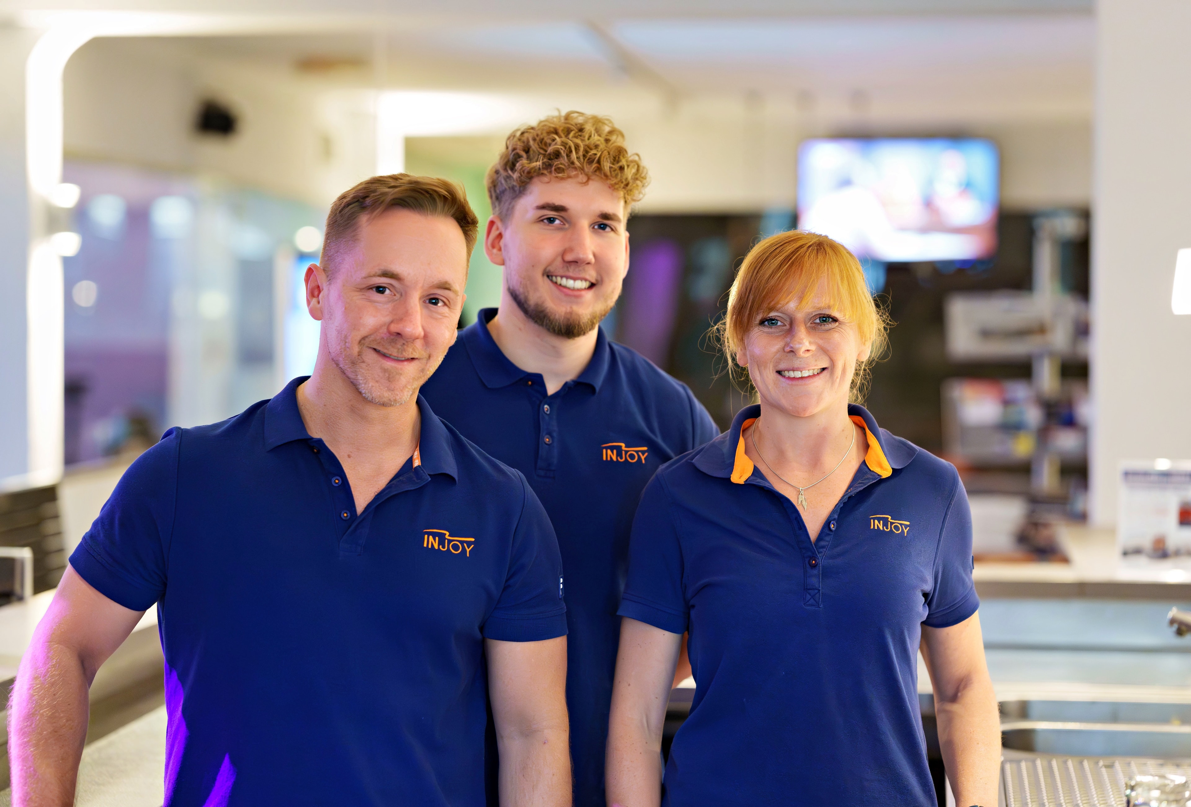 Drei Trainer des INJOY Fitnessstudios in Hagen posieren auf der Trainingsfläche für ein Teamfoto.