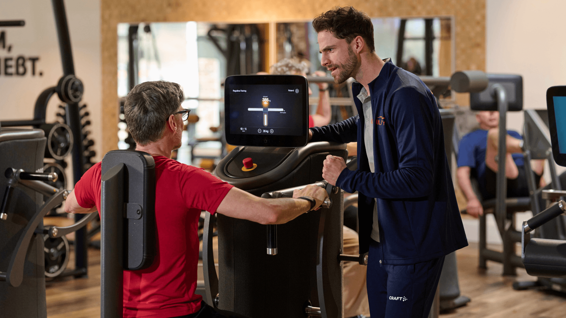 Ein INJOY Trainer motiviert ein Mitglied an einem EGYM Gerät.