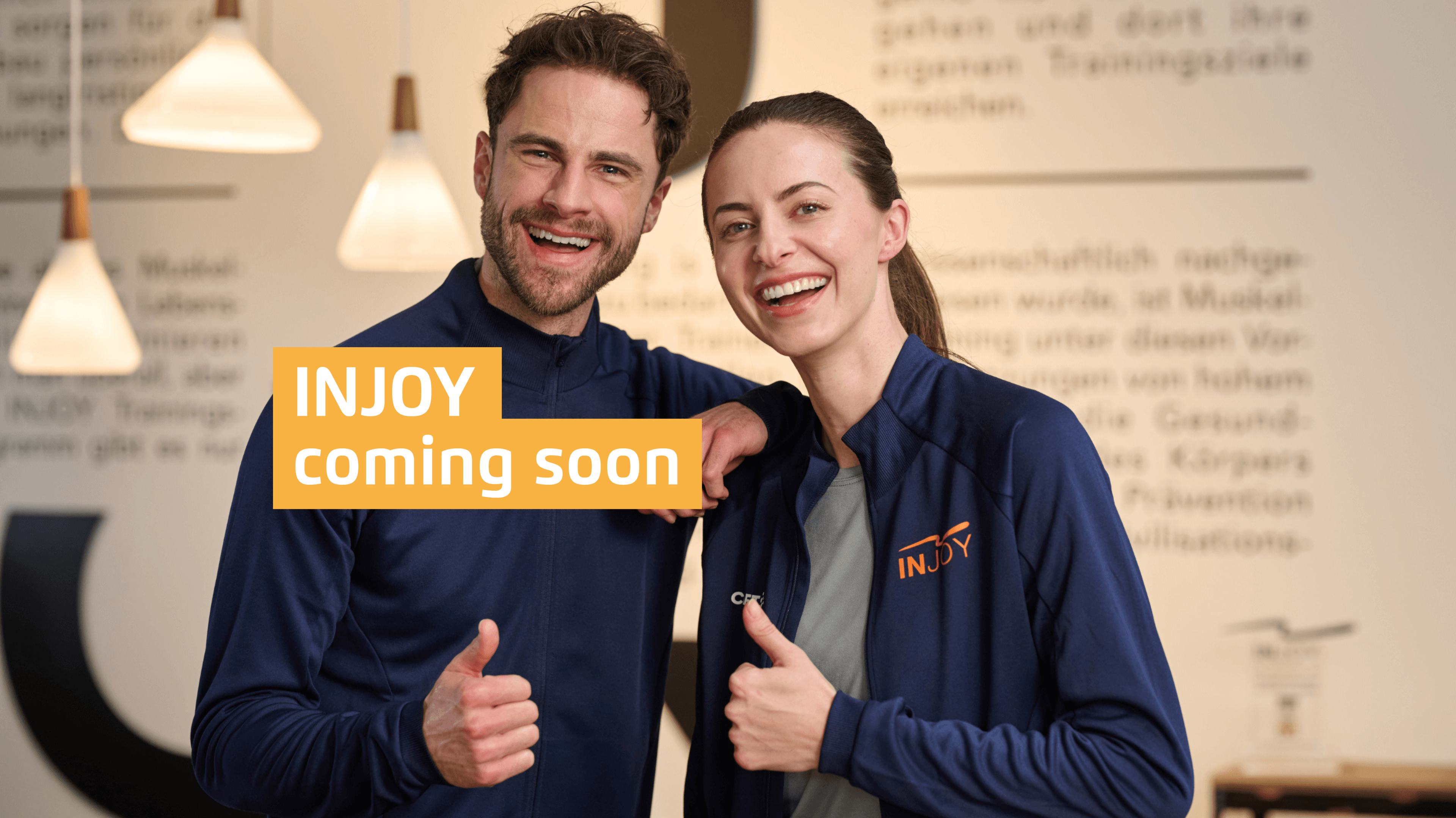 Zwei INJOY Trainer posieren mit Daumen nach oben. Darüber ein Textoverlay "INJOY coming soon", welches das neue INJOY Fitnessstudio in der Nähe anteasert.
