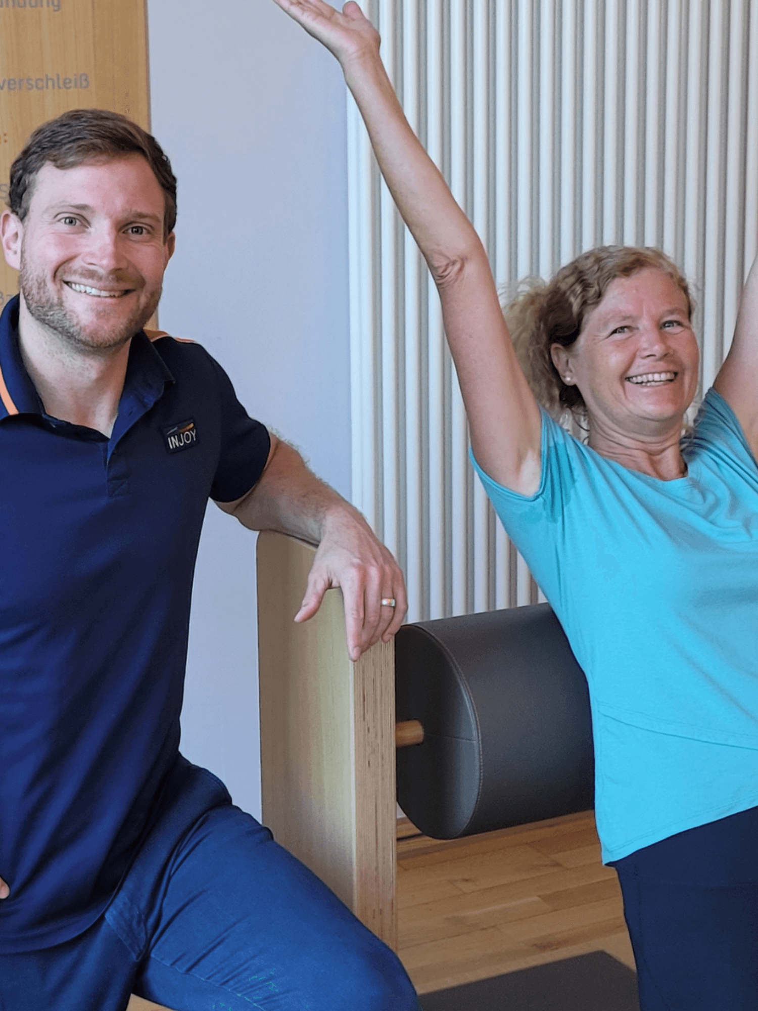 Ein INJOY Mitglied trainiert an einem Five Gerät im INJOY Fitnessstudio in Emmendingen und wird dabei von einem Trainer betreut. Beide lächeln in die Kamera.