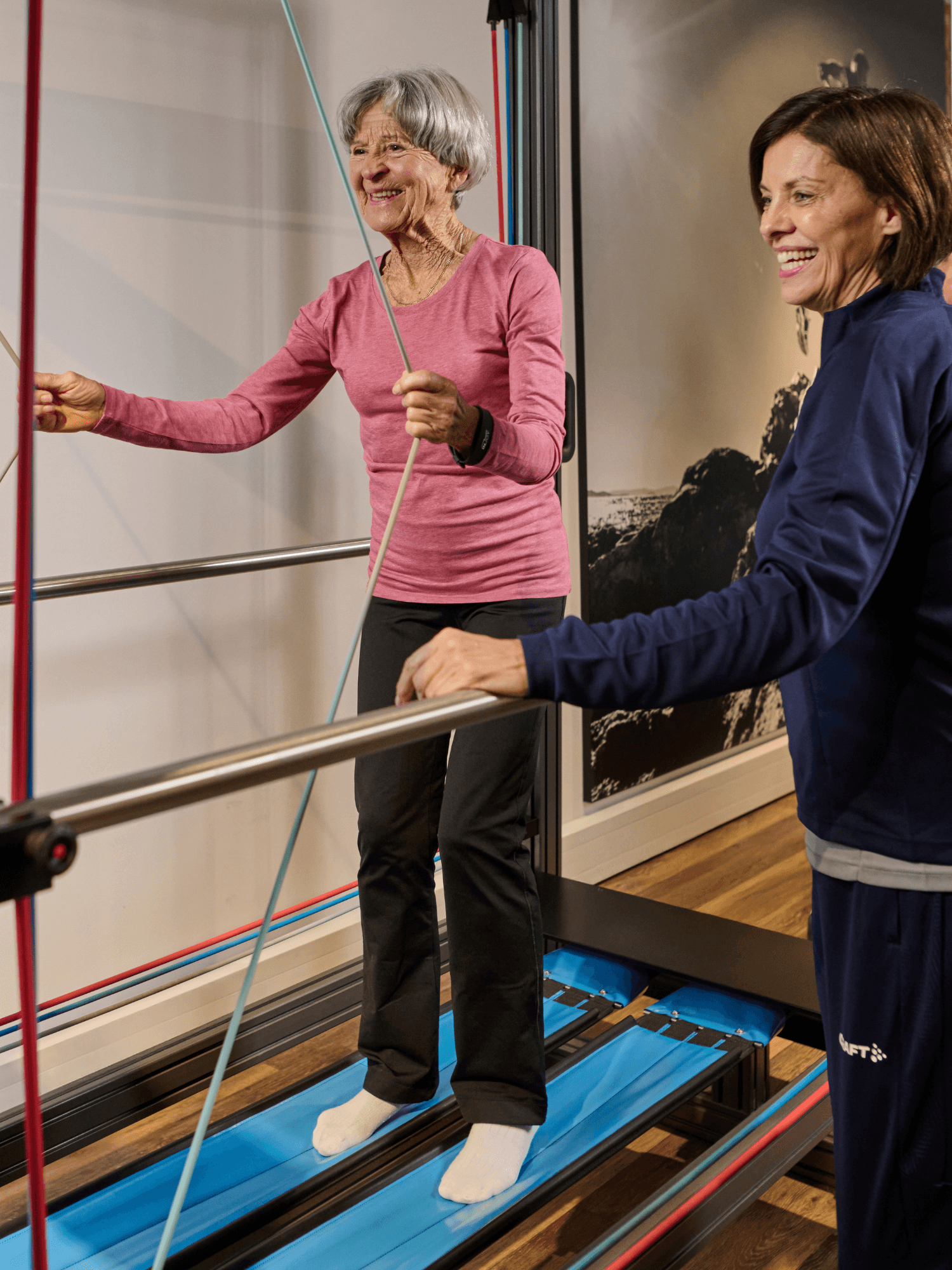 Ein älteres INJOY Mitglied steht auf einem Sensopro Gerät und wird dabei von einer INJOY Trainerin betreut.