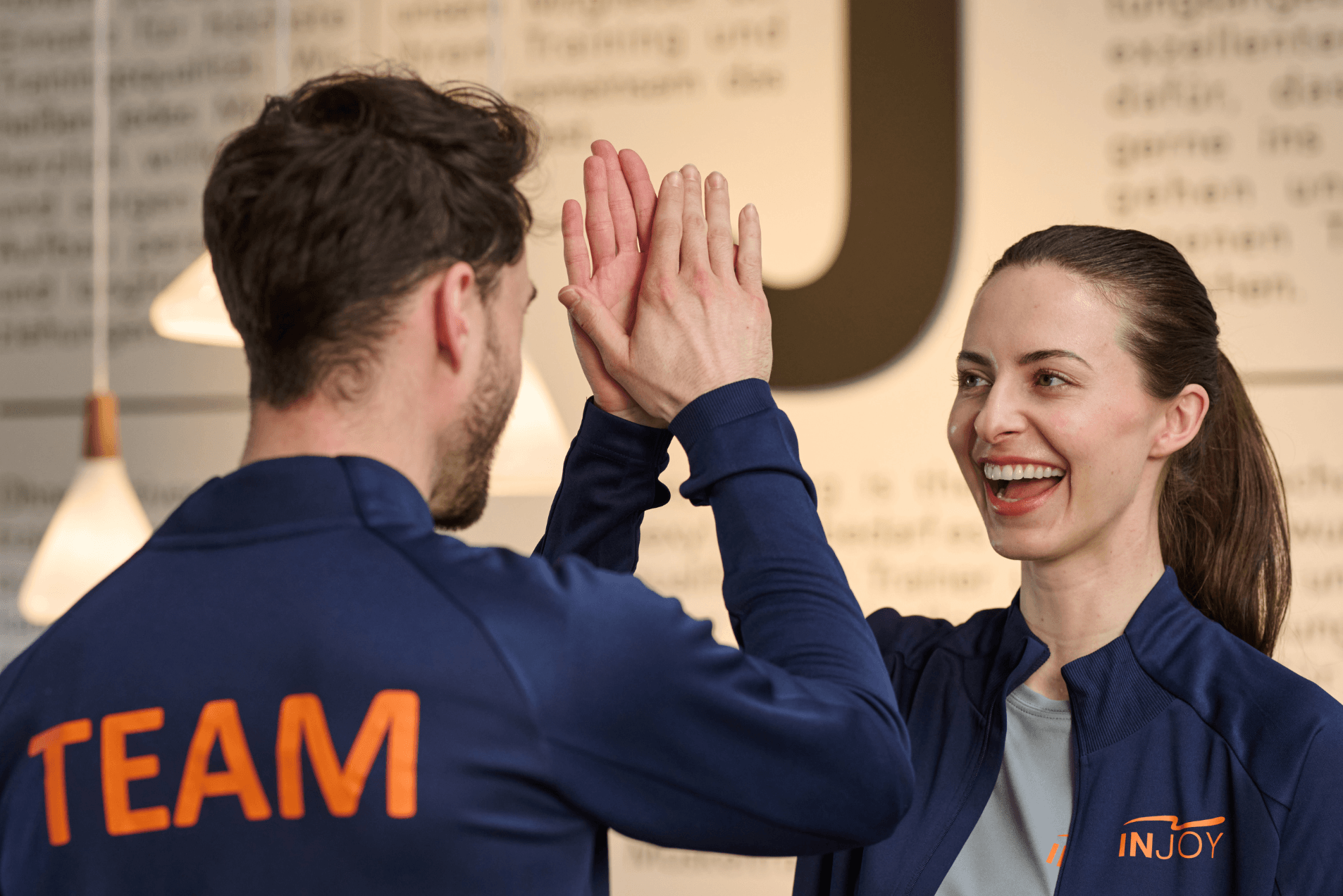 Ein INJOY Trainer und eine INJOY Trainerin lachen sich an und geben sich ein High Five.